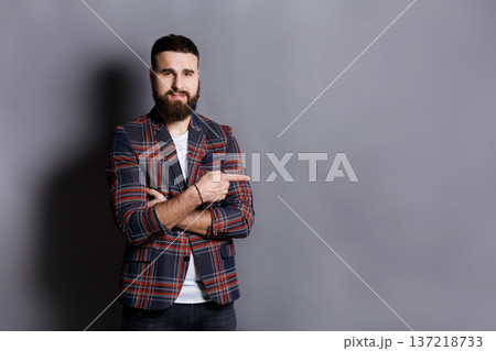 Young confident bearded hipster point away. Serious man gesturing with his finger aside, gray studio background, copy space 137218733