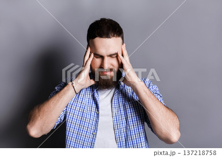 Concentrated bearded man thinking about something, holding fingers on temple, gray studio background. Brainstorm, bad memory, headache concept Concentrated bearded man thinking about something, holding fingers on temple, gray studio background. Brainstorm, bad memory, headache concept 137218758