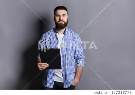 Young serious bearded man standing with folder, preparing for speech or report, gray background, copy space Young serious bearded man standing with folder, preparing for speech or report, gray background, copy space 137218778