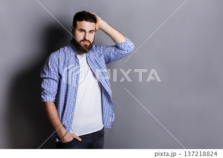Handsome bearded man touching his hair. Young confident guy in relaxed pose, gray studio background. Flirt, seduction concept 137218824