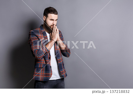 Portrait of hopeful bearded hipster praying. Young guy holding hands clasped near face, looking away, gray studio background, copy space 137218832
