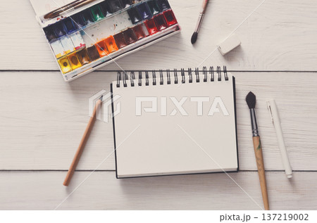 Drawing tools, stationary supplies, workplace of artist. Watercolor paints and blank paper on white wooden desk, top view, flat lay, copy space 137219002