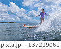 Cheerful Female Surfer Maintains Bold Posture Amidst Vibrant Spray And Sky 137219061