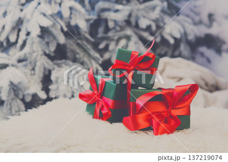 Christmas gifts decorated with red ribbon bows on soft fluffy carpet at blurred snowy fir tree background, closeup, selective focus. Winter holidays concept 137219074