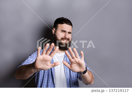 Bearded pushing away with his hands in foreground, expressing his refusal, aversion or repulsion with stopping hand gesture, gray studio background Bearded pushing away with his hands in foreground, expressing his refusal, aversion or repulsion with stopping hand gesture, gray studio background 137219117