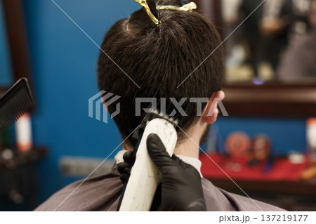 Man getting haircut with trimmer by hairstylist at barbershop, closeup. Modern hair salon 137219177