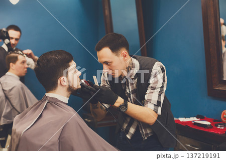Barber styling beard with trimmer at barbershop, closeup. Barbershop for men Barber styling beard with trimmer at barbershop, closeup. Barbershop for men 137219191