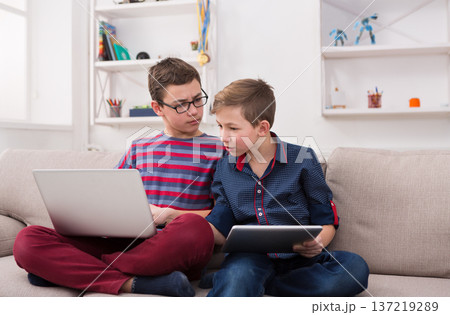 Two male kids with gadgets. Sharing funny content on laptop and digital tablet on sofa at home. Boy friendship and communication concept 137219289