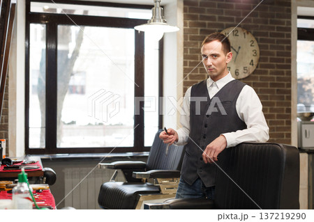 Young barber waits for client, looking at camera. Male hairstylist in barbershop Young barber waits for client, looking at camera. Male hairstylist in barbershop 137219290