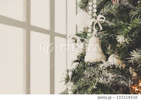 Winter holidays atmosphere background. Closeup of beautifully decorated fir tree with modern baubles, beards, garland and small toy bell . Christmas and new year magic at home, copy space on window Winter holidays atmosphere background. Closeup of beautifully decorated fir tree with modern baubles, beards, garland and small toy bell . Christmas and new year magic at home, copy space on window 137219310