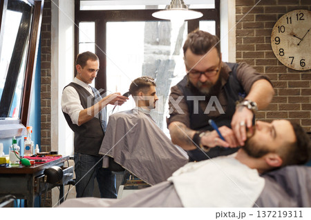 Barbers work in barbershop with clients. Making modern hairstyle in male hair salon Barbers work in barbershop with clients. Making modern hairstyle in male hair salon 137219311