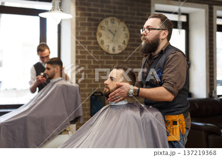 Barbers make haircut to clients at barbershop. Stylish hairdressers in male hair salon Barbers make haircut to clients at barbershop. Stylish hairdressers in male hair salon 137219368
