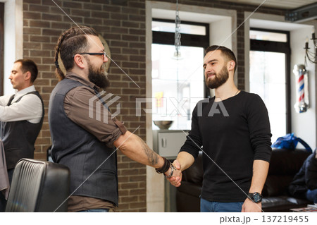 Thankful client and barber shaking hands after haircut. Hairstylist and satisfied customer handshaking at barbershop Thankful client and barber shaking hands after haircut. Hairstylist and satisfied customer handshaking at barbershop 137219455