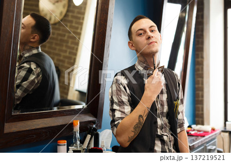 Young elegant barber waits for client, looking at camera. Male hairstylist in barbershop Young elegant barber waits for client, looking at camera. Male hairstylist in barbershop 137219521