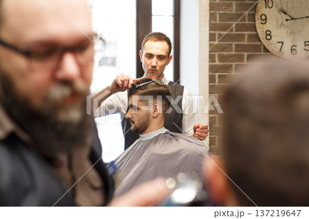 Barbers make haircut to clients at barbershop. Stylish hairdressers in male hair salon Barbers make haircut to clients at barbershop. Stylish hairdressers in male hair salon 137219647