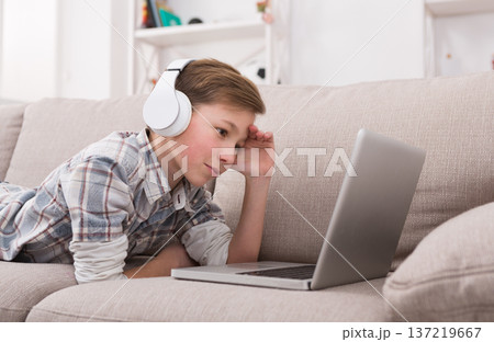 Boy enjoy music from laptop, portrait of dreamy kid in headphones lying on sofa indoors. Relax time at home Boy enjoy music from laptop, portrait of dreamy kid in headphones lying on sofa indoors. Relax time at home 137219667