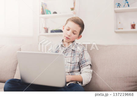 Bored boy with computer on sofa at home. Child trying to find interesting content on the internet, typing on keyboard Bored boy with computer on sofa at home. Child trying to find interesting content on the internet, typing on keyboard 137219668