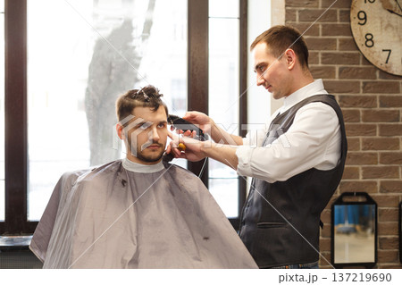 Barber make haircut with trimmer hair clipper in barbershop. Hairstyle in barbershop. Barber make haircut with trimmer hair clipper in barbershop. Hairstyle in barbershop. 137219690