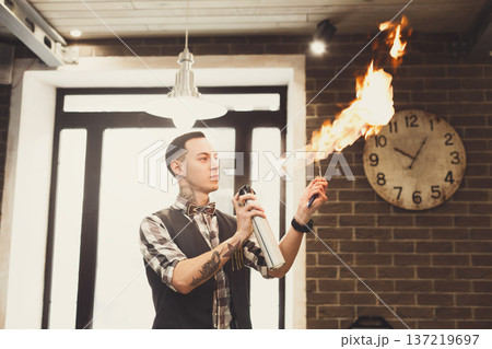 Professional male hairdresser heating the blade of old-fashioned straight razor under stream of fire for smoother shaving. Stylish barber preparing tools for traditional beard shave at barbershop 137219697