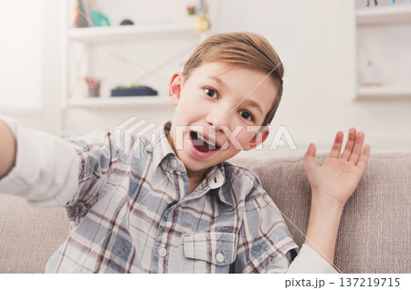 Happy child taking selfie for social networks. Boy at home on sofa in living room Happy child taking selfie for social networks. Boy at home on sofa in living room 137219715