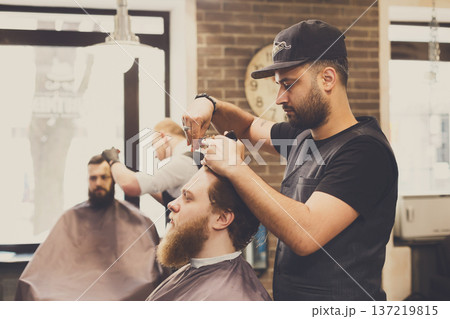 Man getting haircut by hairstylist at barbershop. Stylish barber and client Man getting haircut by hairstylist at barbershop. Stylish barber and client 137219815