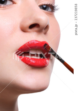 Lips makeup closeup. Apply lipstick with brush. Close-up of female model face with fashion glossy red make-up, beauty concept isolated 137219858