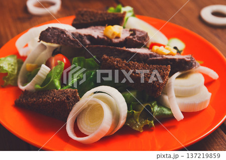 Healthy eating concept. Fresh organic salad with greens, rye bread, leek and steamed meat on orange plate at wooden background 137219859