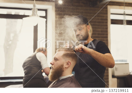 Man getting haircut by hairstylist at barbershop. Stylish barber and client Man getting haircut by hairstylist at barbershop. Stylish barber and client 137219911