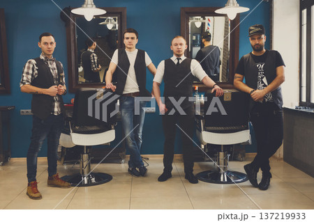 Team of barbers in modern barbershop. Four masculine male hairstylists standing indoors at workplace in hair salon Team of barbers in modern barbershop. Four masculine male hairstylists standing indoors at workplace in hair salon 137219933