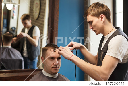 Young barbers cuts hair with trimmer in barbershop. Making modern hairstyle in male hair salon 137220031