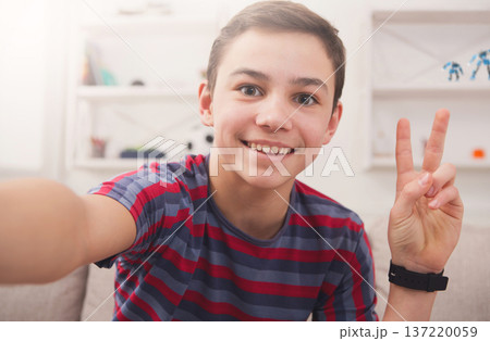 Happy teenager making selfie for social networks. Boy at home on sofa in living room Happy teenager making selfie for social networks. Boy at home on sofa in living room 137220059