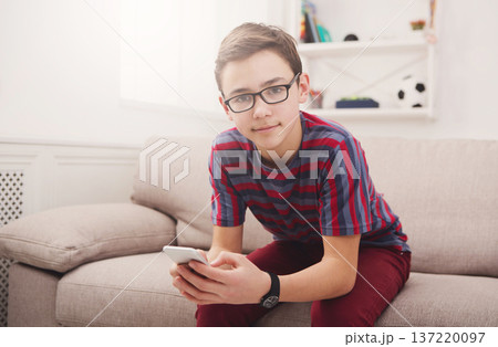 Teenage boy at home with mobile phone, seats on sofa in living room 137220097