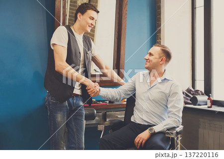 Thankful client and barber shaking hands after haircut. Hairstylist and satisfied customer handshaking at barbershop Thankful client and barber shaking hands after haircut. Hairstylist and satisfied customer handshaking at barbershop 137220116