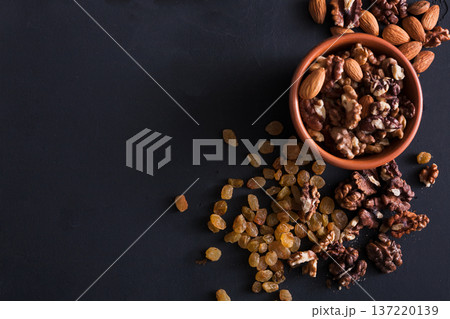 Nuts and raisins snack at black background. Healthy source of fat for vegans and vegetarians. Closeup, selective focus on almonds and copy space 137220139