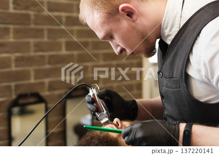 Man getting haircut with trimmer by hairstylist at barbershop. Modern hair salon. Closeup of hairstylist at work Man getting haircut with trimmer by hairstylist at barbershop. Modern hair salon. Closeup of hairstylist at work 137220141
