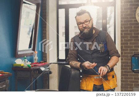 Experienced bearded barber at workplace in barbershop. Professional stylish hairdresser waiting for client at hair salon 137220159