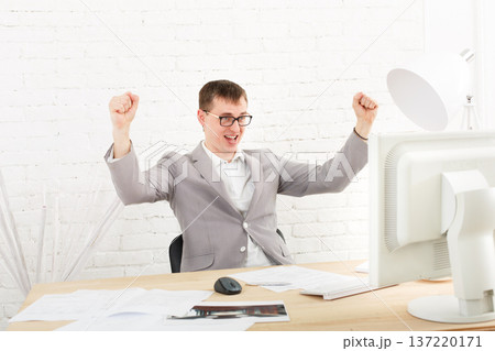 Winner businessman happy, succesful, in white modern office interior, sitting at computer table. Office worker in eye glasses, job in internet. High key, soft tone. Businessman win prize, gambling. 137220171