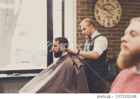 Barbers work in barbershop with bearded clients. Making modern hairstyle in male hair salon Barbers work in barbershop with bearded clients. Making modern hairstyle in male hair salon 137220248