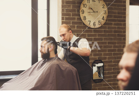 Man getting haircut by hairstylist at barbershop. Stylish barber and client 137220251