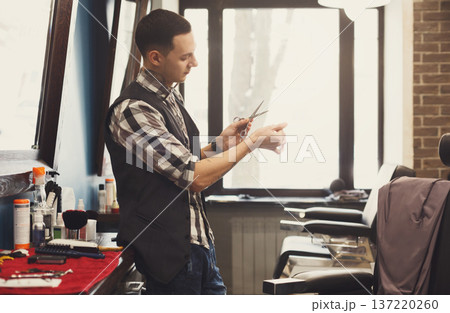 Experienced bearded barber at workplace in barbershop. Professional stylish hairdresser waiting for client at hair salon Experienced bearded barber at workplace in barbershop. Professional stylish hairdresser waiting for client at hair salon 137220260
