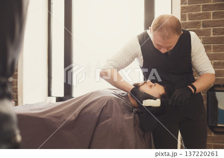 Barber styling beard to client at barbershop. Stylish hairdresser in male hair salon 137220261