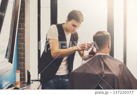 Barbers cuts hair in barbershop. Making modern hairstyle in male hair salon 137220377