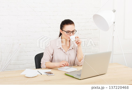 Middle aged businesswoman working in white modern office interior, with laptop. Female office work, woman in eye glasses, drinking coffee. High key, soft tone. woman in office. Middle aged businesswoman working in white modern office interior, with laptop. Female office work, woman in eye glasses, drinking coffee. High key, soft tone. woman in office. 137220468