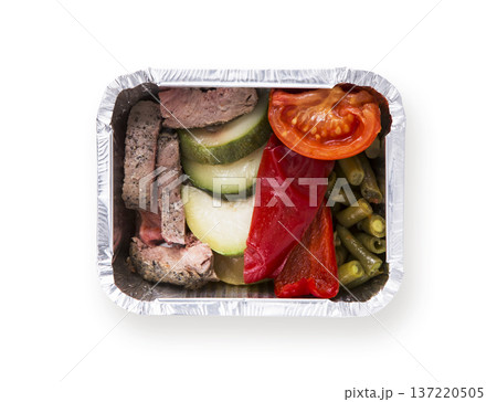 Healthy food in foil box isolated at white background. Dietary restaurant food delivery. Steamed meat with backed vegetable salad of asparagus, zucchini, tomatoe and pepper, top view 137220505