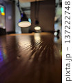 A blurred close-up of a wooden table, exhibiting a shiny, polished surface with visible grain lines. Two pendant lamps emit a soft, warm glow 137222748