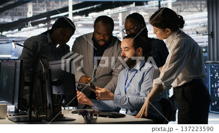 Data center system administrators performing maintenance on supercomputers used for AI processing. Team managing server hub rigs used for deep learning training, looking over business charts, camera A Data center system administrators performing maintenance on supercomputers used for AI processing. Team managing server hub rigs used for deep learning training, looking over business charts, camera A 137223590
