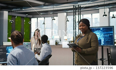 Happy female engineer in office automating repetitive tasks using AI scripts. Jolly african american developer using artificial intelligence to speed up feature implementation, camera A 137223596