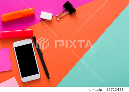 A smartphone is centered on a bright, vibrant office workspace surrounded by various stationery items like sticky notes, highlighters, a binder clip, and a pen, showcasing a creative setup. A smartphone is centered on a bright, vibrant office workspace surrounded by various stationery items like sticky notes, highlighters, a binder clip, and a pen, showcasing a creative setup. 137224514