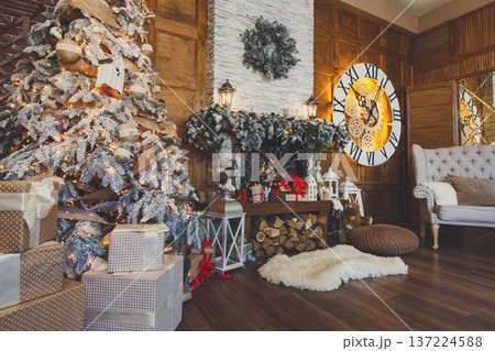 Beautiful christmas interior. Warm room with fireplace, decorated christmas tree, lots of presents and huge clock on wooden wall. Cozy home for winter holidays, copy space, side view Beautiful christmas interior. Warm room with fireplace, decorated christmas tree, lots of presents and huge clock on wooden wall. Cozy home for winter holidays, copy space, side view 137224588