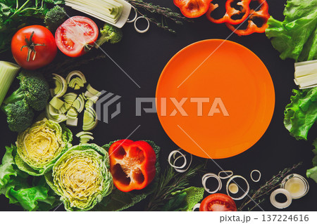 Healthy vegetable food on black background. Fresh organic peppers, tomato, cabbage and other meals with empty orange plate, copy space 137224616